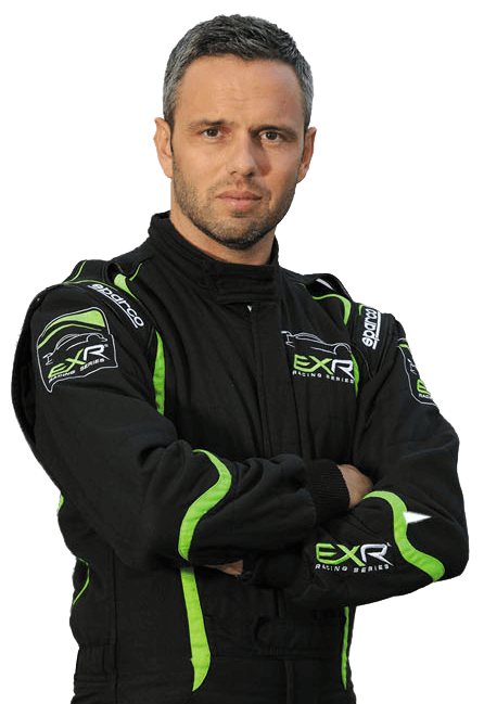 Race car driver in a black jumpsuit with green accents and "EXR" logo, stands confidently with arms crossed, looking determined against a neutral backdrop.