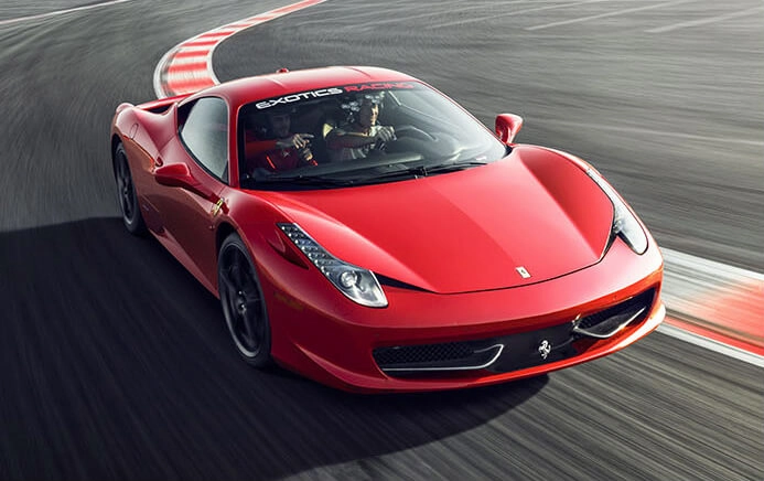 A sleek red sports car speeds around a racetrack curve. The dynamic motion and sharp design convey excitement and thrill.