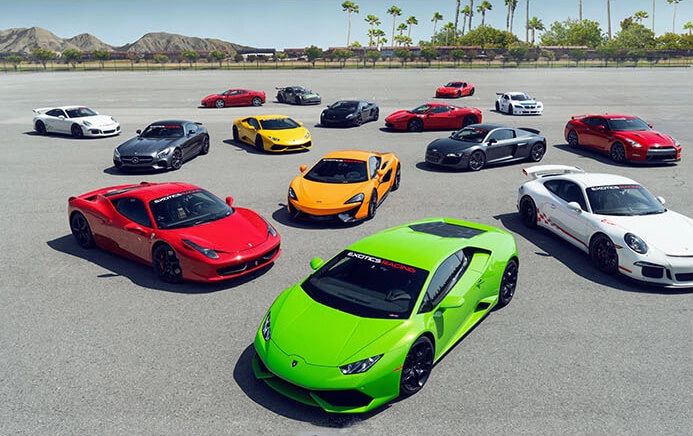 Cluster of vibrant sports cars, including a prominent green Lamborghini, arranged on an expansive asphalt lot under a clear sky, evoking excitement.