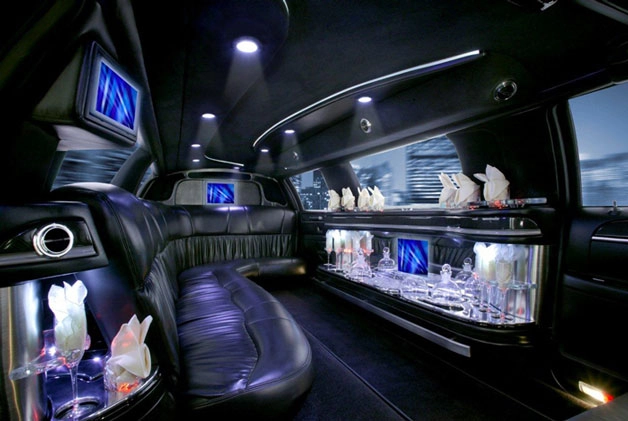 Luxurious limousine interior with black leather seats, ambient blue lighting, and multiple screens. Decorative glasses and napkins create an elegant tone.